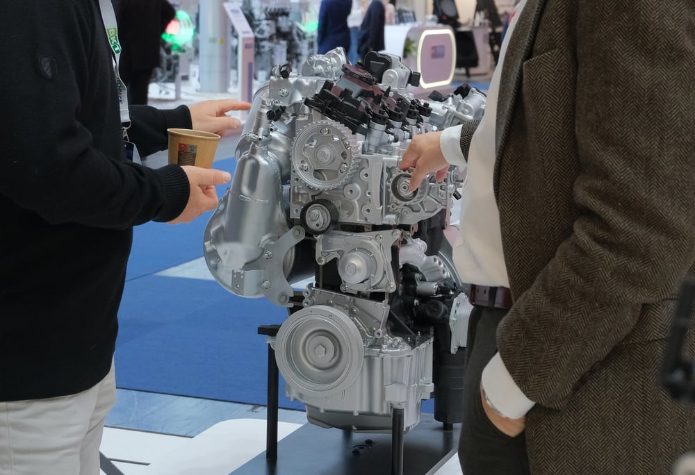 Two people, only torsos and arms viewable, having a conversation around an engine