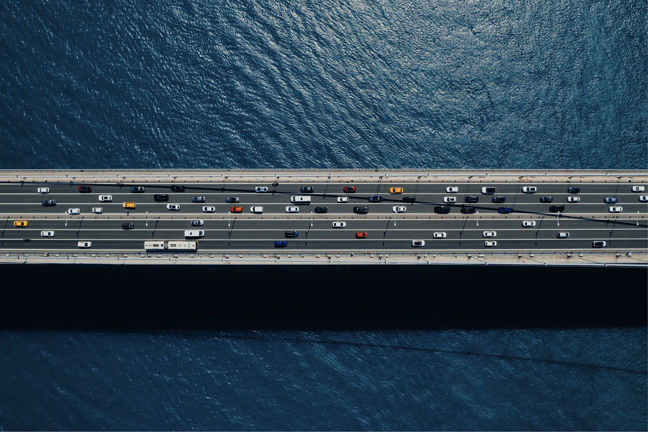 a bridge with six lanes of vehicles in both directions going over water with a perspective from above